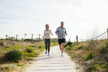 Happy mature couple running on pathway at beach - EBSF03242