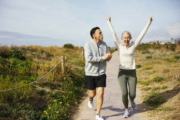 Mature man applauding by woman jogging at beach - EBSF03243