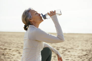 Frau sitzt und trinkt aus einer Wasserflasche am Strand - EBSF03249