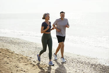 Smiling mature couple jogging together near shore at beach - EBSF03254