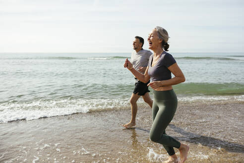 Glückliches reifes Paar lachend und im Wasser laufend am Strand - EBSF03265