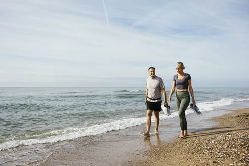 Mature couple walking on sand near sea at beach - EBSF03267