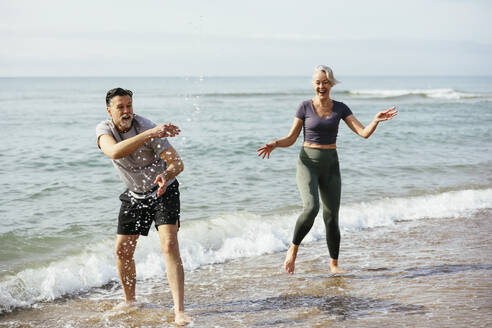 Playful couple enjoying in sea at beach - EBSF03271