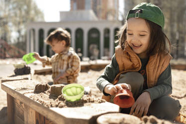 Lächelnder Junge spielt mit Sand auf einem Spielplatz an einem sonnigen Tag - ANAF01374