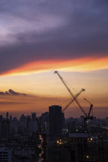 Thailand, Bangkok, Wolken über dem Stadtzentrum in der Abenddämmerung mit Industriekränen im Hintergrund - IKF00408