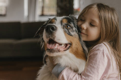 Mädchen umarmt Australian Shepherd zu Hause - VIVF00768