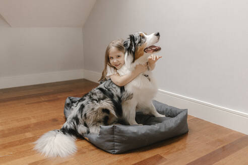 Mädchen umarmt Australian Shepherd auf Haustierbett zu Hause - VIVF00777