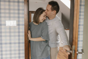 Man kissing woman standing by doorway at home - VIVF00780