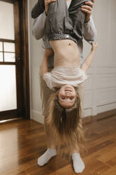 Father holding daughter upside down at home - VIVF00786