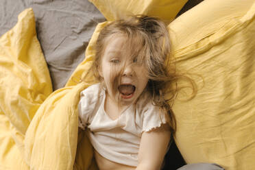 Blondes Mädchen schreit auf dem Bett bei Kissen zu Hause - VIVF00791