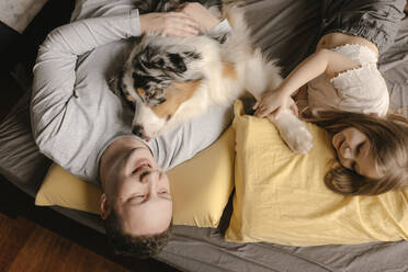 Father and daughter relaxing with Australian Shepherd on bed at home - VIVF00792