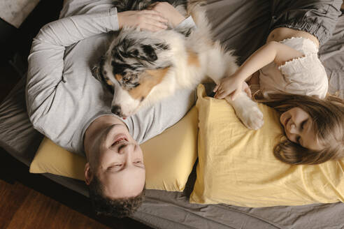 Vater und Tochter entspannen sich mit Australian Shepherd auf dem Bett zu Hause - VIVF00792