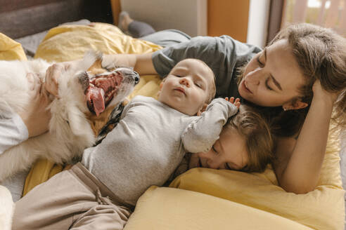 Mutter und Kinder spielen mit Australian Shepherd auf dem Bett zu Hause - VIVF00794