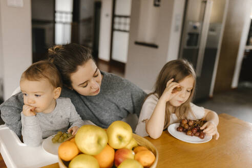Mutter mit Sohn und Tochter essen frisches Obst zu Hause - VIVF00797