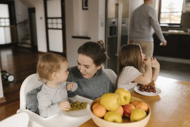 Mutter mit Kindern isst Obst am Esstisch - VIVF00798