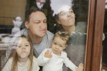 Familie drückt Nasen gegen Fenster im Haus - VIVF00819