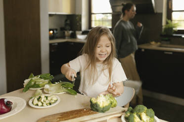 Fröhliches Mädchen schneidet Gemüse in der Küche - VIVF00820