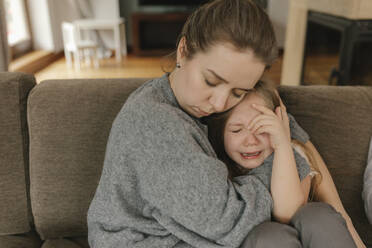 Mother consoling crying daughter on sofa - VIVF00824