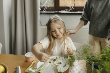 Girl doing creativity with vegetables on plate by mother at home - VIVF00844