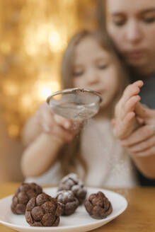 Mutter, die ihrer Tochter hilft, Puderzucker auf Schokoladentannenzapfen zu streuen - VIVF00849