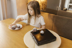 Mädchen dekoriert Schokoladenkuchen mit Tannenzapfen zu Hause - VIVF00850