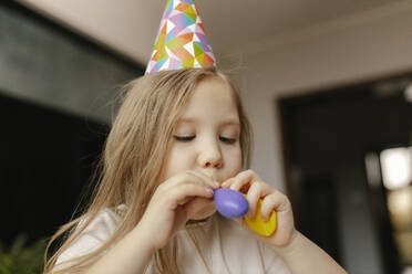 Girl wearing party hat inflating balloon at home - VIVF00857