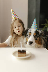 Mädchen bläst Geburtstagskerze auf Kuchen am Tisch aus - VIVF00859