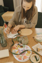 Young woman pouring paint in palette at home - VIVF00864