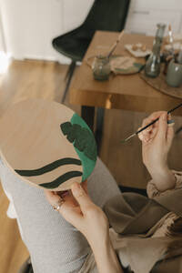 Frau malt auf Holzbrett sitzend am Tisch - VIVF00871