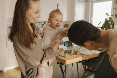 Happy woman carrying playful daughter touching hair of man at home - VIVF00874