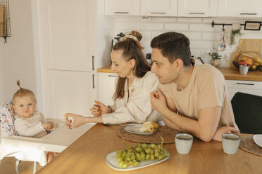 Father and mother with cute daughter eating fruit at home - VIVF00882