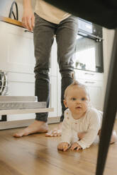 Cute baby girl crawling on floor by father loading utensils in dishwasher at home - VIVF00890