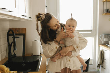 Smiling mother carrying cute daughter in kitchen at home - VIVF00896