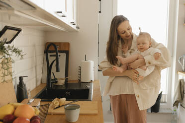 Smiling mother carrying daughter by kitchen counter at home - VIVF00900