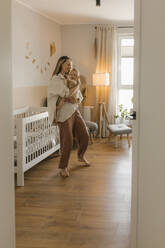 Mother rocking baby daughter in arms at nursery bedroom - VIVF00901