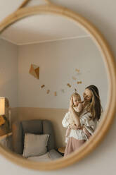 Smiling mother carrying baby daughter reflecting in mirror at home - VIVF00904