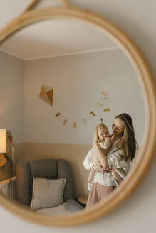 Lächelnde Mutter mit ihrer kleinen Tochter, die sich im Spiegel zu Hause spiegelt - VIVF00904