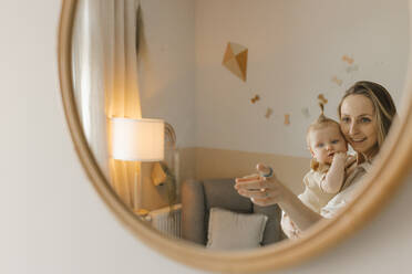 Glückliche Mutter mit ihrer kleinen Tochter, die sich im Spiegel zu Hause spiegelt - VIVF00905