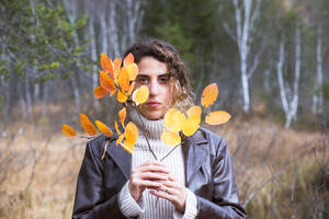 Ernste Frau hält einen Zweig mit Herbstblättern im Wald - HHF05891