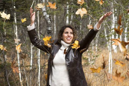 Glückliche Frau spielt mit Herbstblättern im Wald - HHF05892