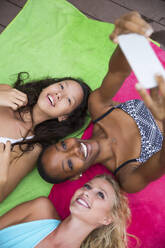 Friends taking selfie through smart phone lying on colorful blanket - IKF00416