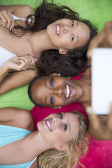 Fröhliche Damen halten den Moment mit einem Selfie fest, während sie sich auf einer bunten und kuscheligen Decke entspannen - IKF00418