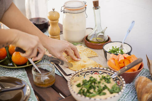 Hände, die fermentiertes Brot schneiden, umgeben von gesundem Essen in Schüsseln und veganen Produkten - PCLF00456