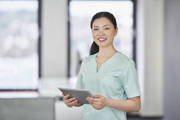 Portrait of smiling nurse in scrubs holding digital tablet - RORF03454
