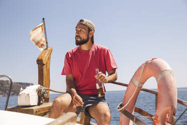 Mann mit Bierflasche auf dem Bug eines Schiffes sitzend - PCLF00486