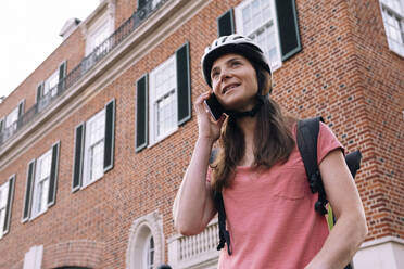 Delivery woman talking on smart phone in front of building - AMWF01306