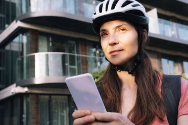 Nachdenkliche Lieferfrau mit Smartphone vor einem Gebäude - AMWF01310
