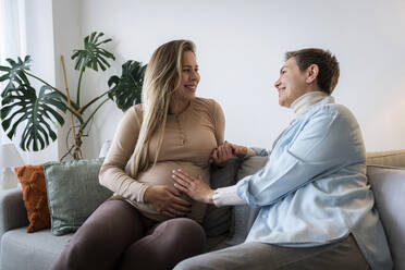 Senior woman with pregnant daughter sitting on sofa at home - AAZF00398