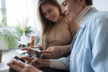 Senior woman looking at ultrasound photos with pregnant daughter at home - AAZF00400