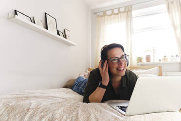 Nachdenklicher Freiberufler mit Laptop, der zu Hause auf dem Bett liegt - ASGF03568